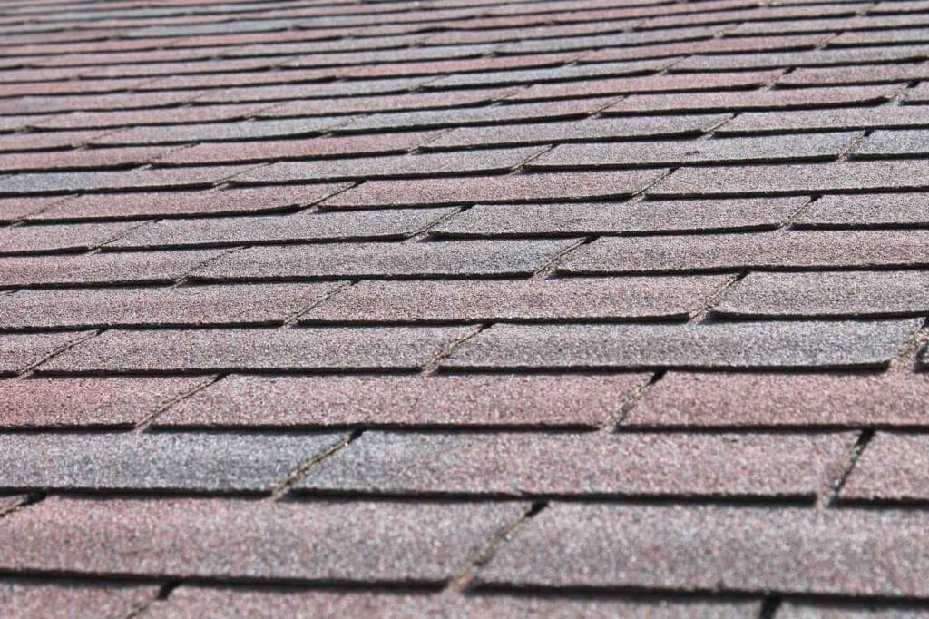 Close-up of a roof covered with gray asphalt shingles in Morris County, NJ. The shingles are arranged in a horizontal pattern, overlapping each other, and appear slightly weathered.
