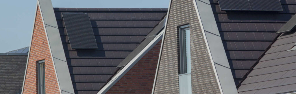 Three modern houses with steep, triangular roofs are lined up. The roofs, installed by a roofing contractor in Morris County NJ, feature dark solar panels and are covered in either dark shingles or bricks. Each house façade showcases narrow windows, emphasizing the sleek architectural design.