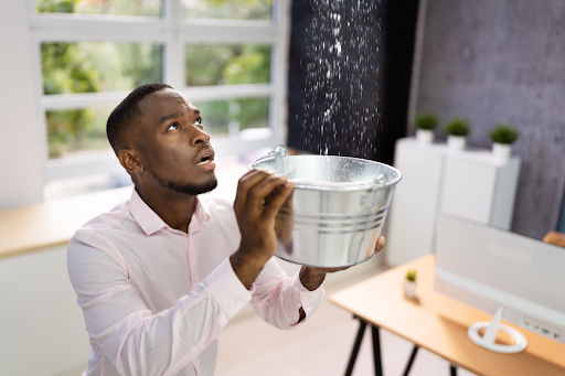 Man holding a bucket underneath a leaking roof